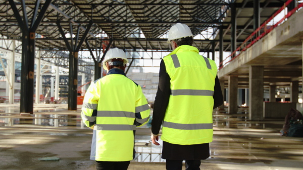 Rear view of man and woman engineers walking on construction site, talking.