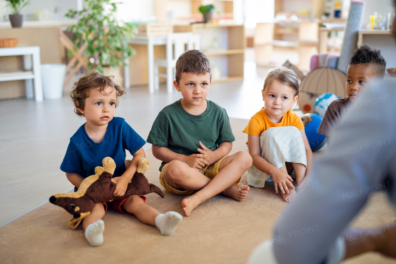 A group of small nursery school children sitting on floor indoors in classroom.