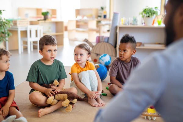 A group of small nursery school children sitting on floor indoors in classroom.