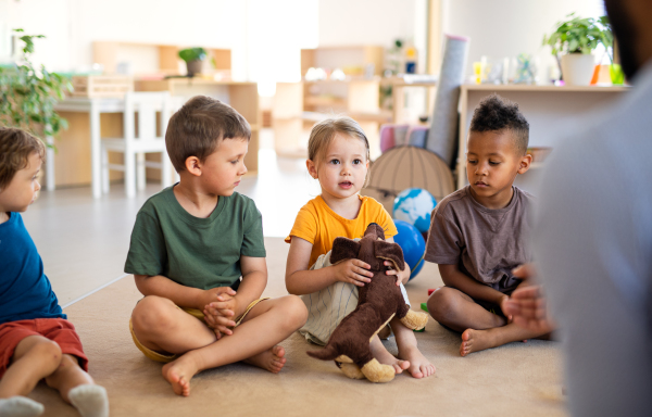 A group of small nursery school children sitting on floor indoors in classroom.