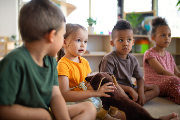 A group of small nursery school children sitting on floor indoors in classroom, listening to teacher.