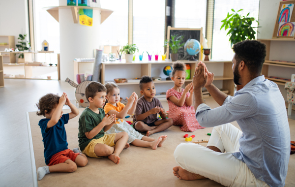 A group of small nursery school children with man teacher sitting on floor indoors in classroom, playing.