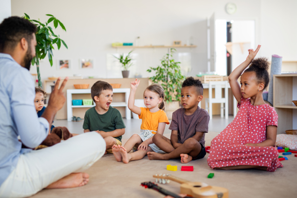 A group of small nursery school children sitting on floor indoors in classroom.