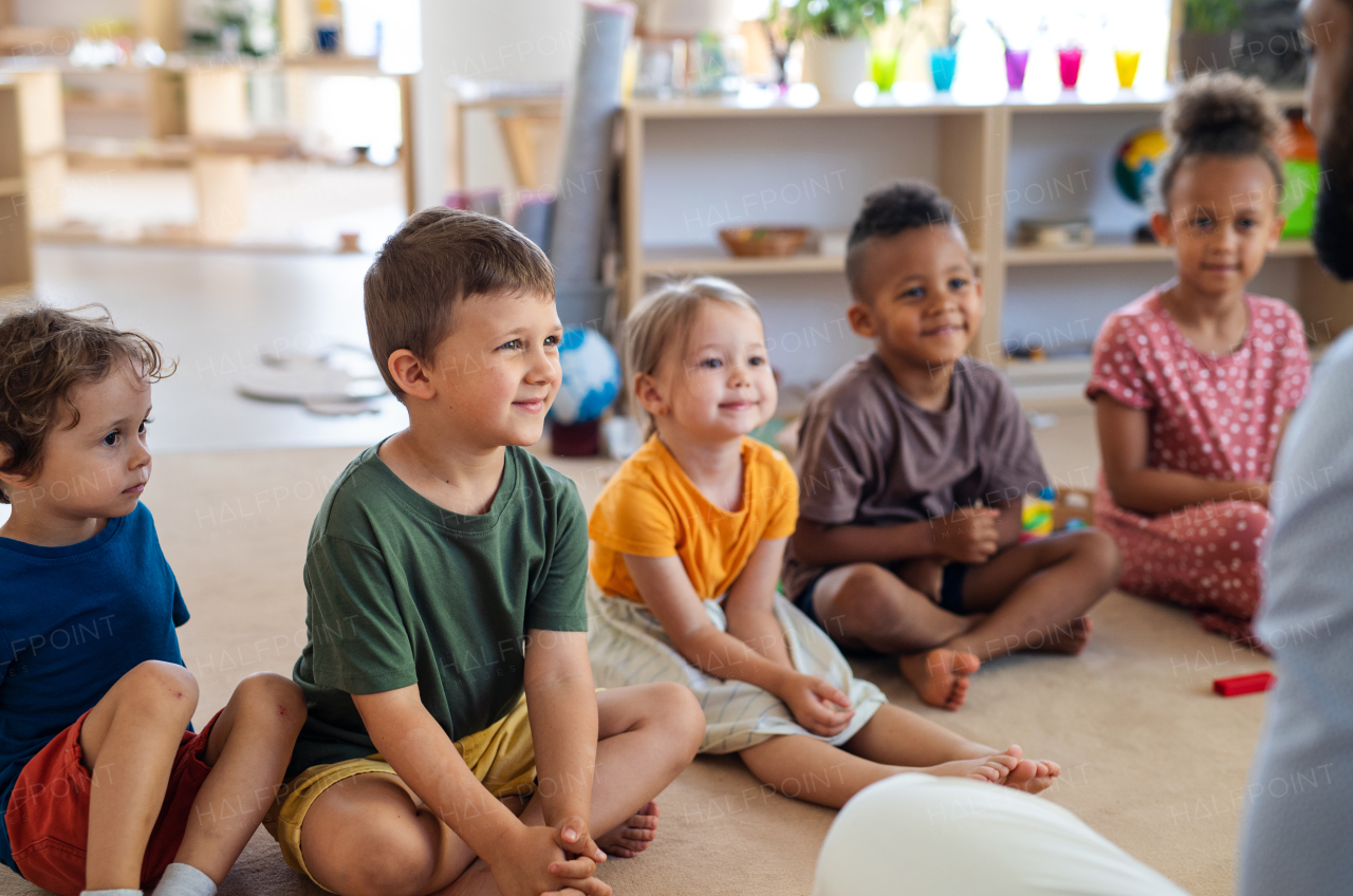 A group of small nursery school children sitting on floor indoors in classroom.