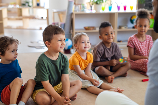 A group of small nursery school children sitting on floor indoors in classroom.