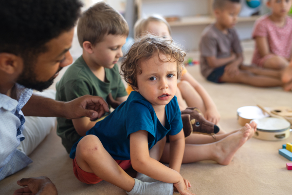 A man teacher talking to small unhappy boy indoors in classroom, comforting him.