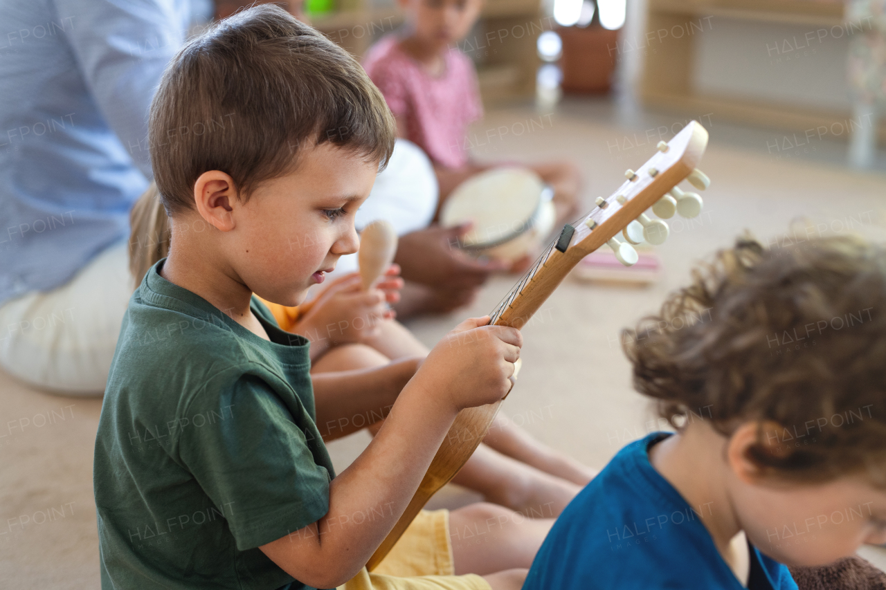 A group of small nursery school children sitting on floor indoors in classroom, playing musical instruments.