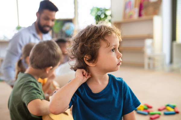 A portrait of small boy with classmateas and teacher indoors in classroom.