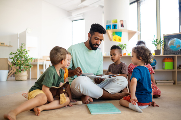 A group of small nursery school children with man teacher sitting on floor indoors in classroom, having lesson.