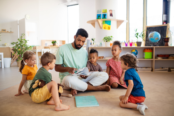 A group of small nursery school children with man teacher sitting on floor indoors in classroom, having lesson.