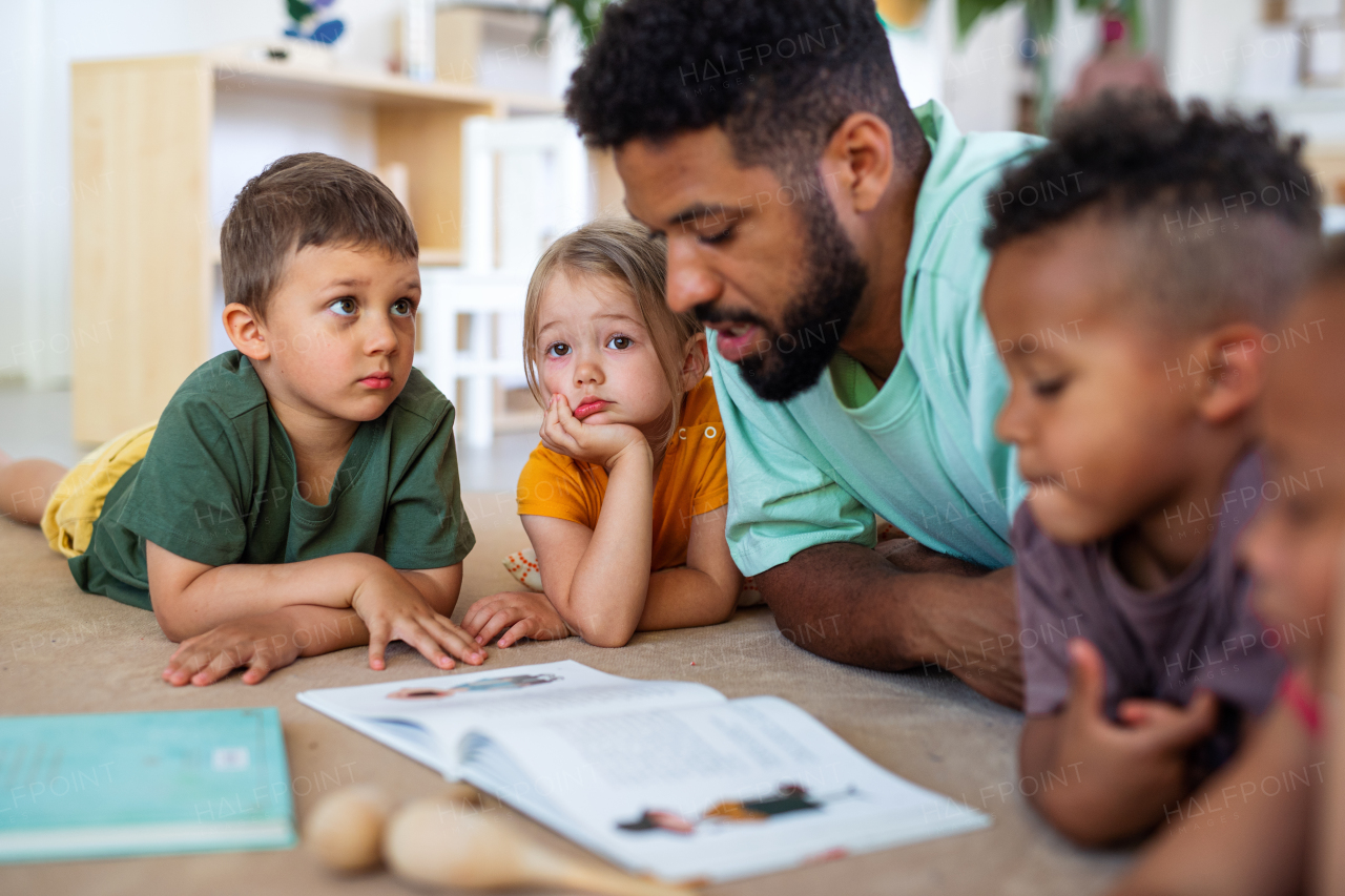 A group of small nursery school children with man teacher on floor indoors in classroom, reading book.