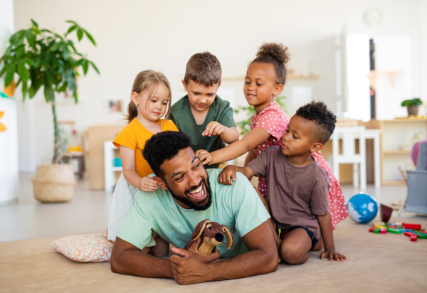 A group of small nursery school children with man teacher sitting on floor indoors in classroom, playing.