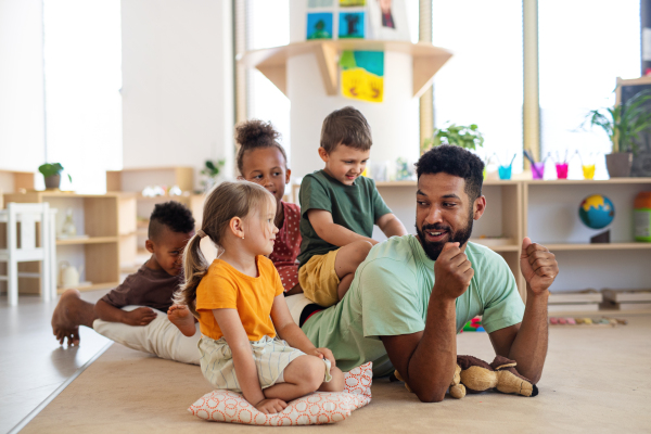 A group of small nursery school children with man teacher sitting on floor indoors in classroom, playing.