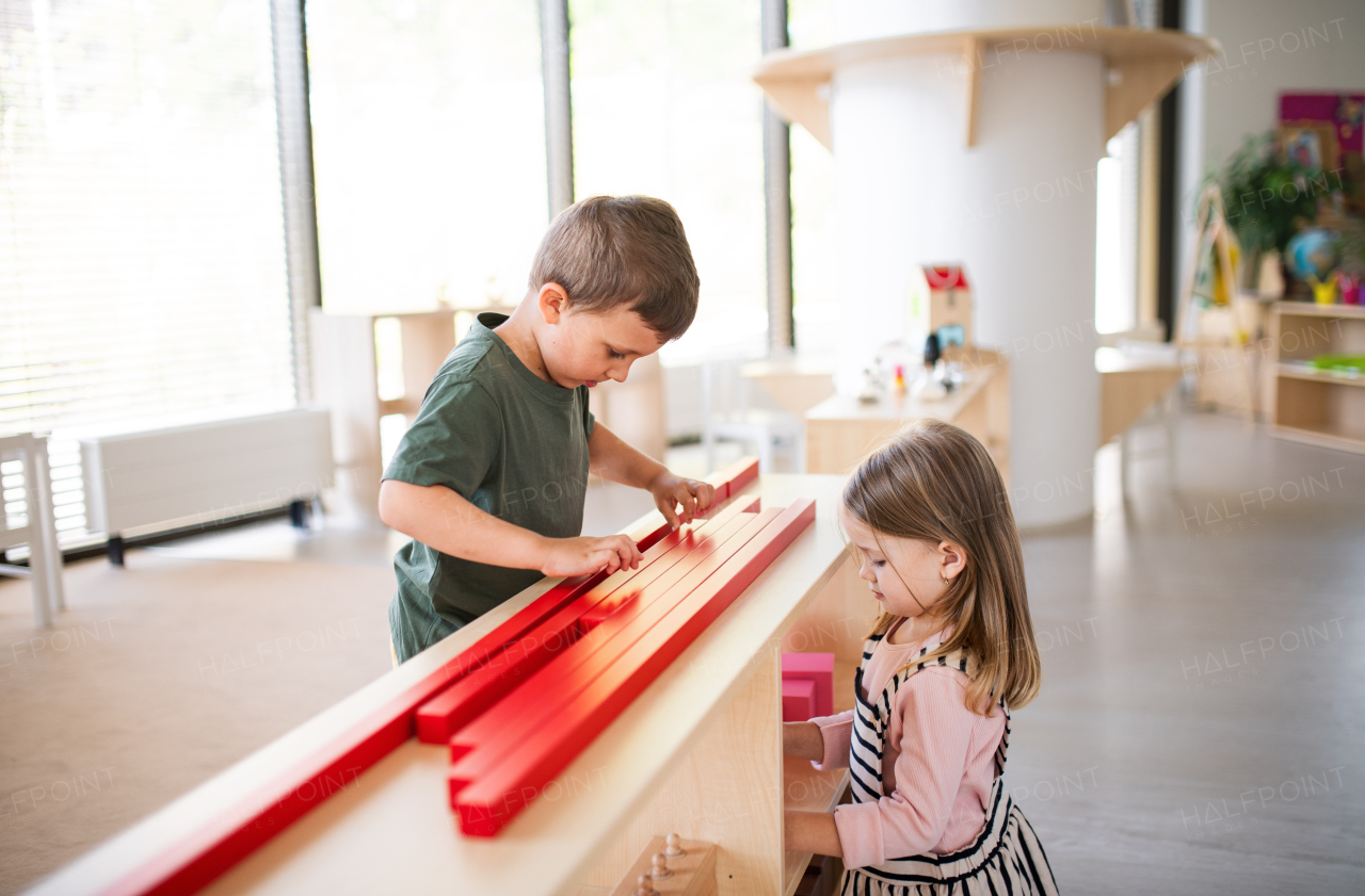 A group of small nursery school children playing indoors in classroom, montessori learning.