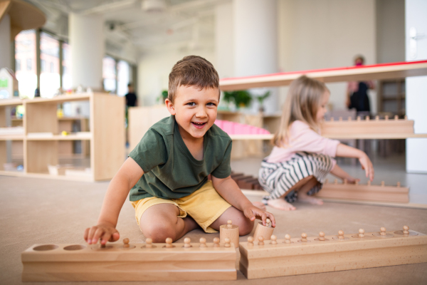 A group of small nursery school children playing indoors in classroom, montessori learning.