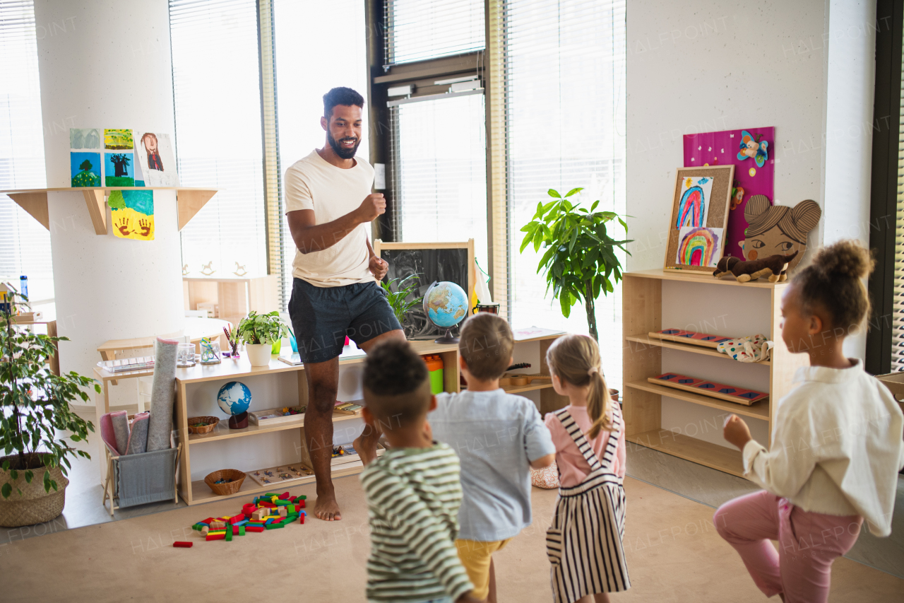 A group of small nursery school children with man teacher standing indoors in classroom, doing exercise.