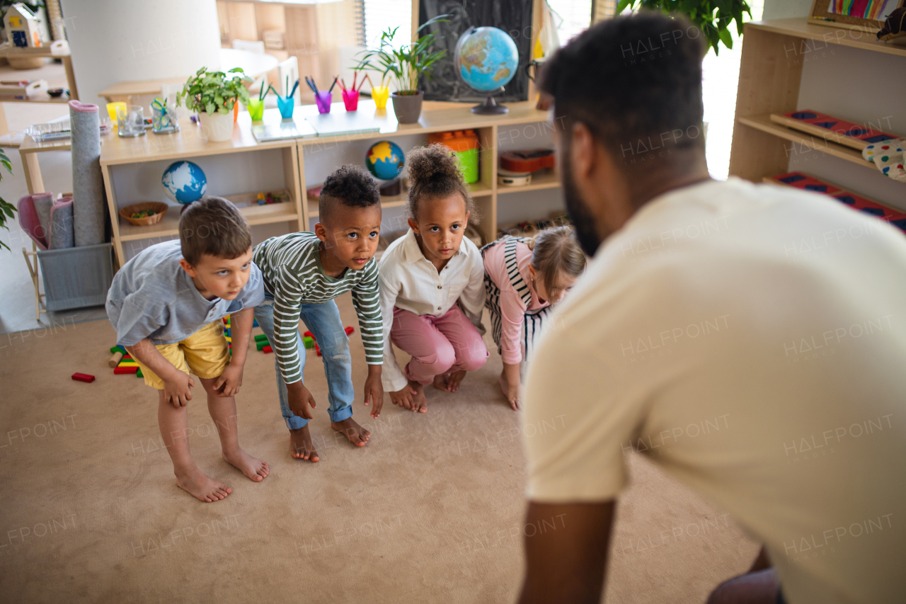 A group of small nursery school children with man teacher indoors in classroom, doing exercise.