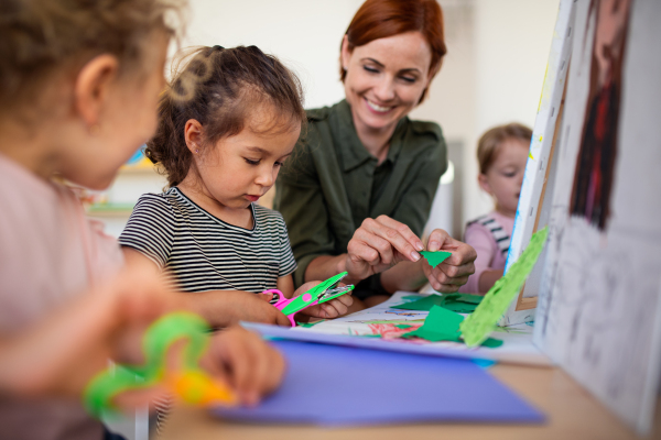 A group of small nursery school children with teacher indoors in classroom, art and craft concept.