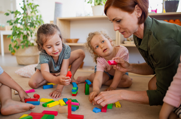 A group of small nursery school children with teacher on floor indoors in classroom, playing.