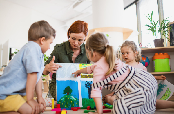 A group of small nursery school children with teacher on floor indoors in classroom, learning.