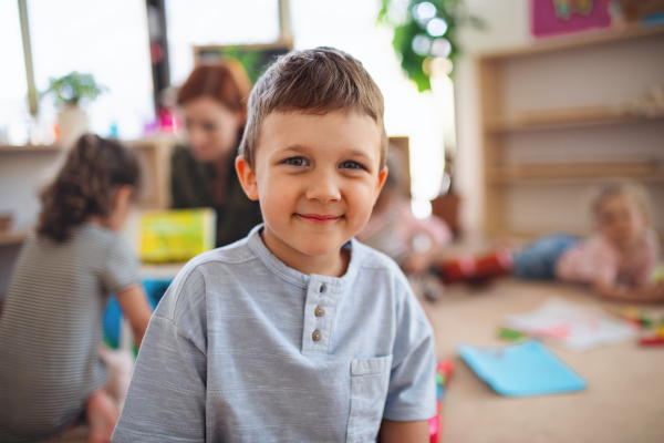 A portrait of small nursery school boy indoors in classroom, looking at camera.