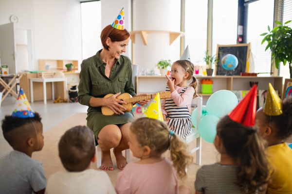 A group of small nursery school children with teacher on floor indoors in classroom, celebration concept.