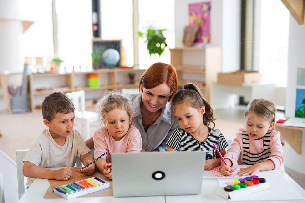 A group of small nursery school children with teacher indoors in classroom, using laptop.