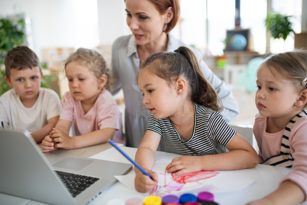 A group of small nursery school children with teacher indoors in classroom, using laptop.