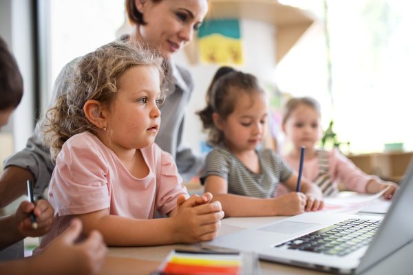 A group of small nursery school children with teacher indoors in classroom, using laptop.