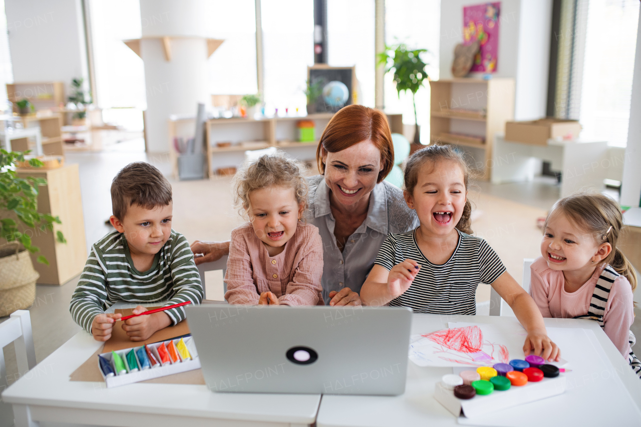 A group of small nursery school children with teacher indoors in classroom, using laptop.