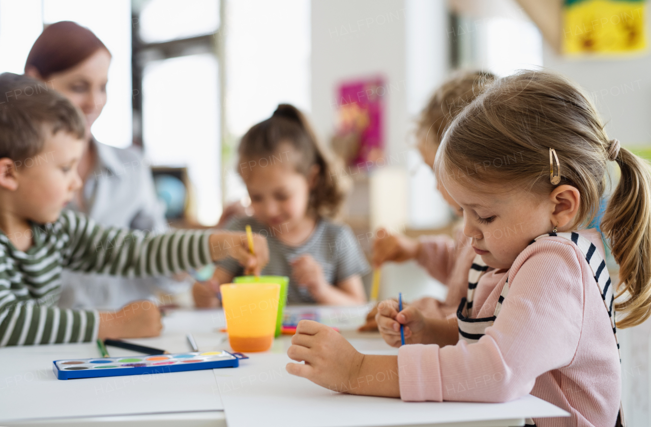 A group of small nursery school children with teacher indoors in classroom, painting.