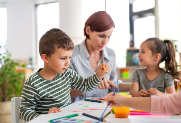 A group of small nursery school children with teacher indoors in classroom, painting.