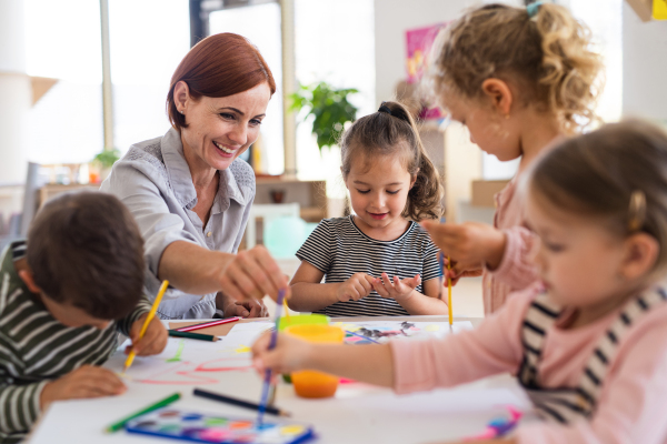 A group of small nursery school children with teacher indoors in classroom, painting.