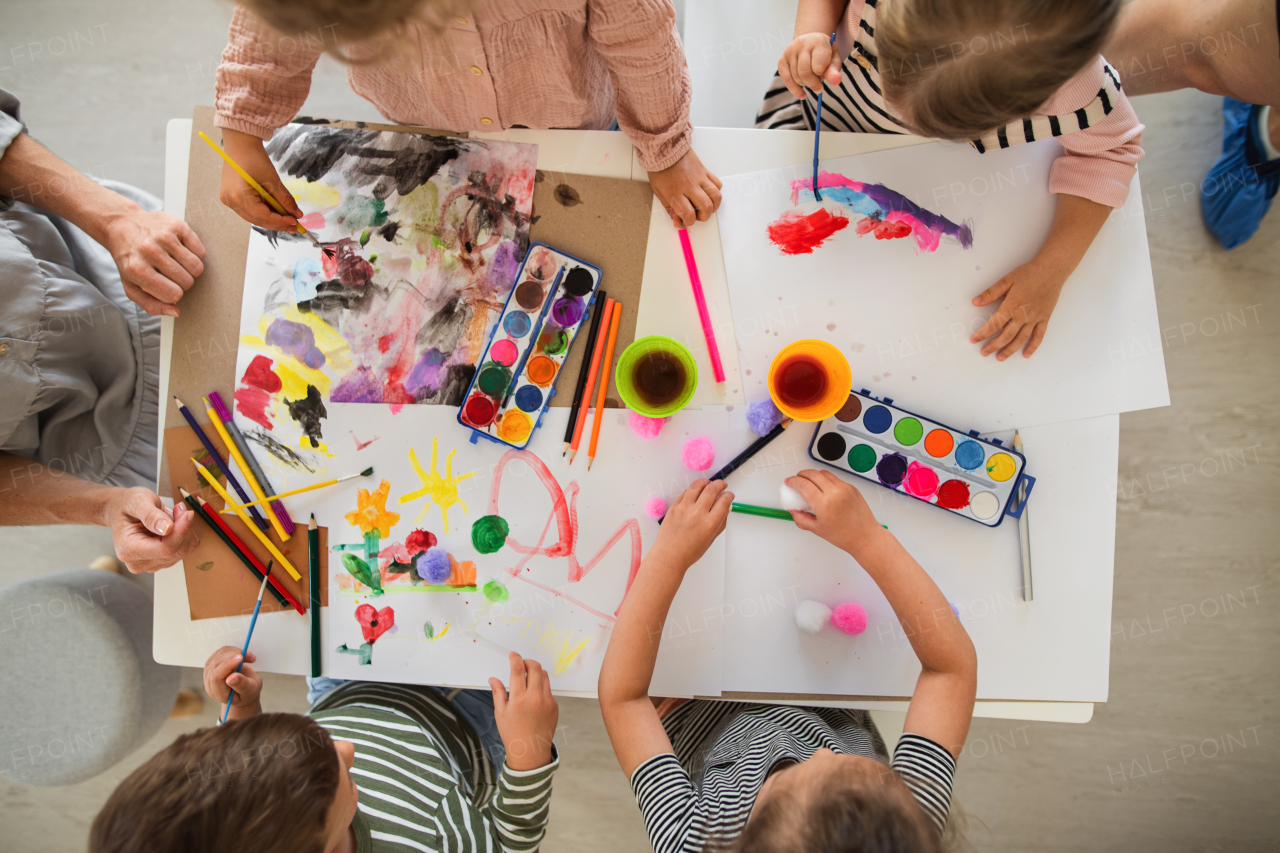 A top view of group of small nursery school children with teacher indoors in classroom, painting.