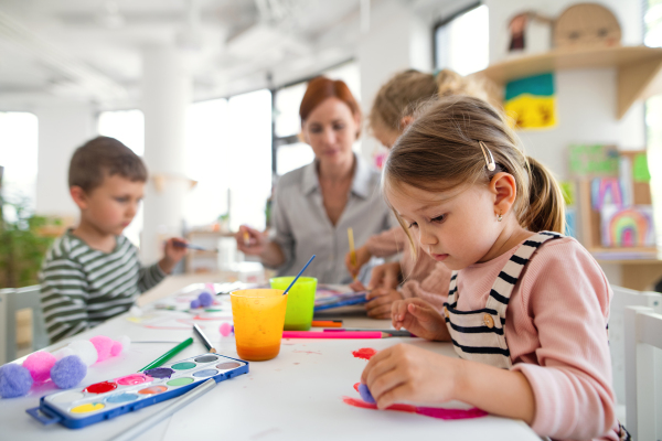 A group of small nursery school children with teacher indoors in classroom, painting.