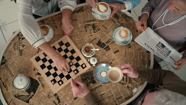 Senior friends enjoying time together and playing chess indoors in a cafe, directly above view.