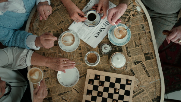 Top view of senior friends sitting indoors in a cafe drinking coffee or tea together.