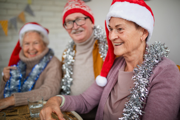 Happy senior friends sitting indoors in a community center and celebrating Christmas.