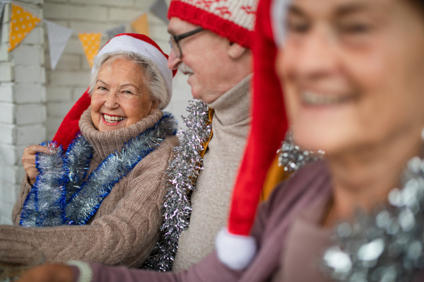 Happy senior friends sitting indoors in a community center and celebrating Christmas.