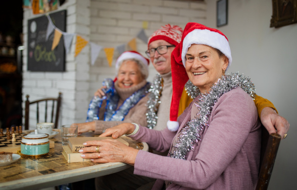 Happy senior friends sitting indoors in a community center and celebrating Christmas.