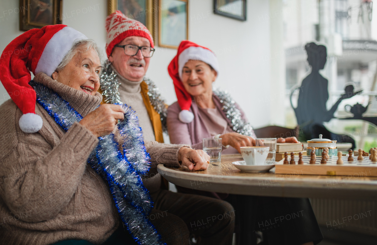 Happy senior friends sitting indoors in a community center and celebrating Christmas.