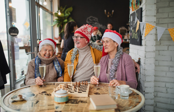 Happy senior friends sitting indoors in a cafe drinking champagne and celebrating Christmas.