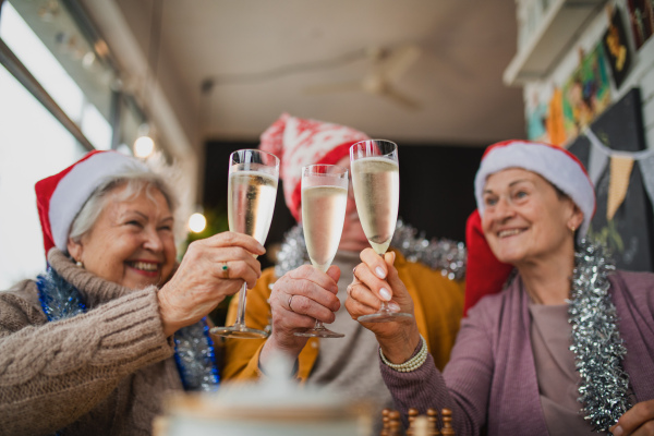 Happy senior friends sitting indoors in a cafe clinking champagne glasses and celebrating Christmas.