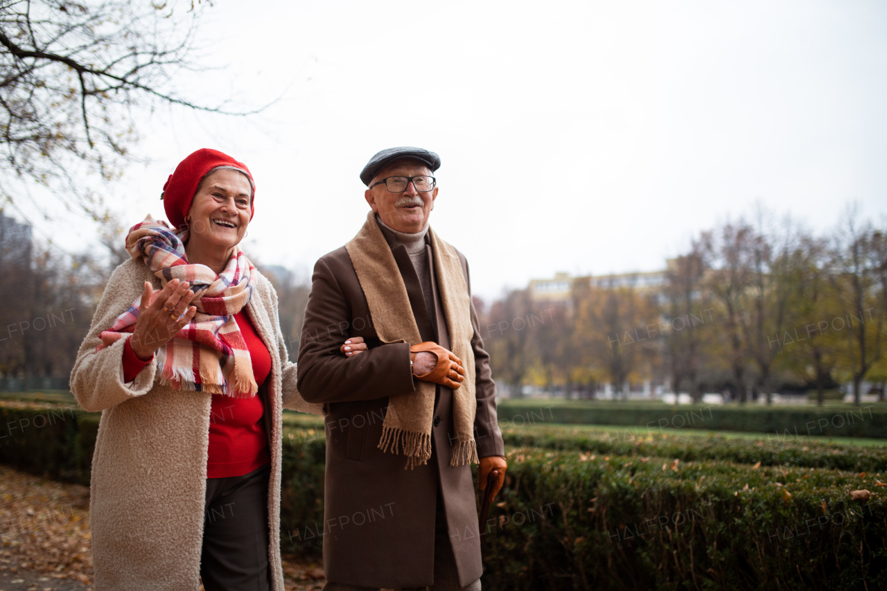 A happy senior couple on walk outdoors in town park in autumn.