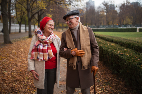 A happy senior couple on walk outdoors in town park in autumn.