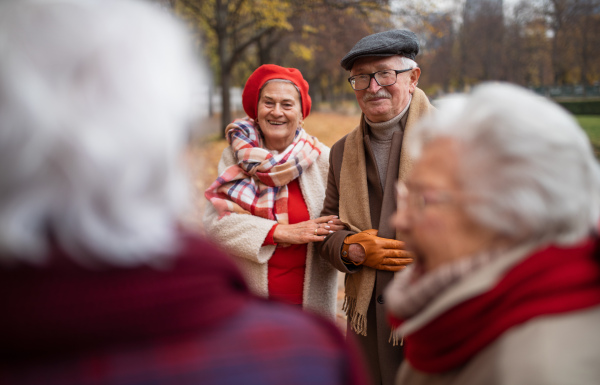 A group of happy senior friends on walk outdoors in town park in autumn, talking and laughing.