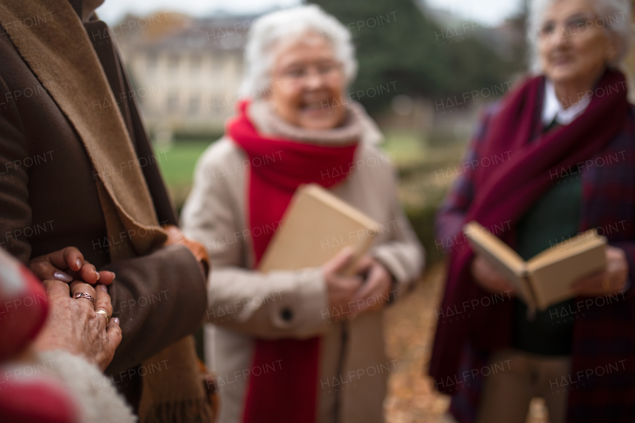 A group of happy senior friends with book on walk outdoors in park in autumn, reading and talking.