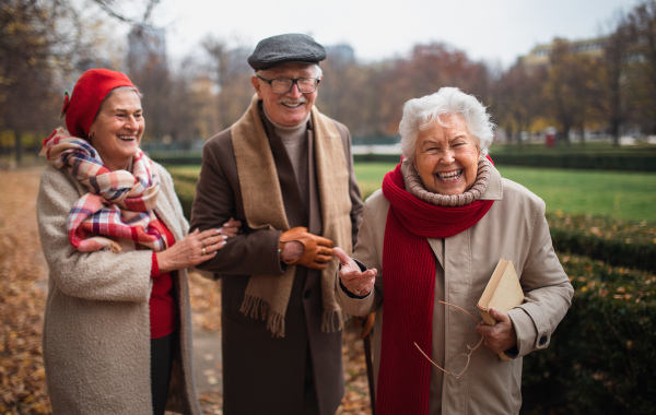 A group of happy senior friends on walk outdoors in town park in autumn, looking at camera.