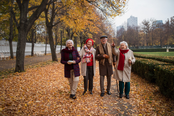 A group of happy senior friends with books on walk outdoors in park in autumn, talking and laughing