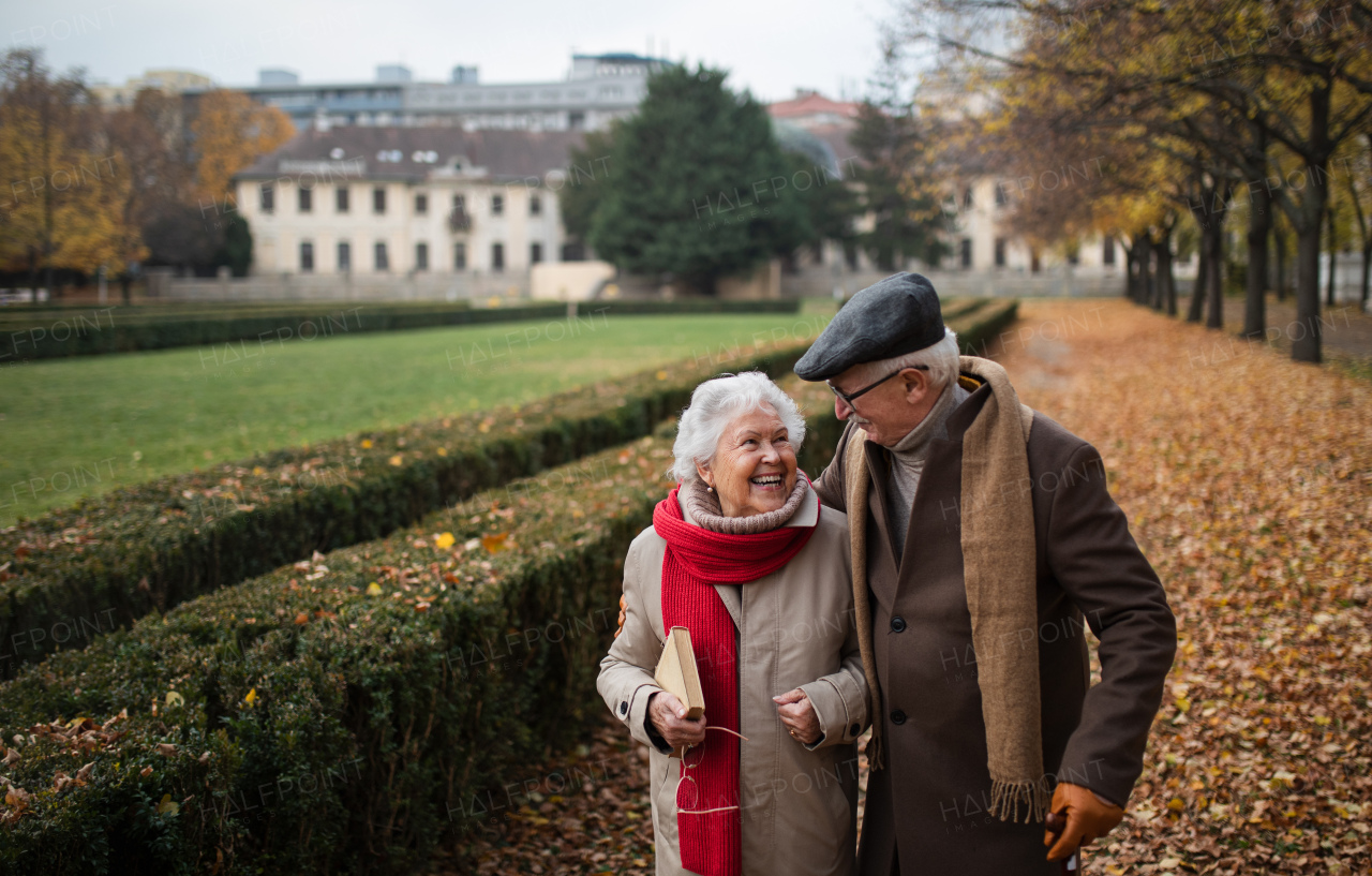 A happy senior couple on walk outdoors in town park in autumn.